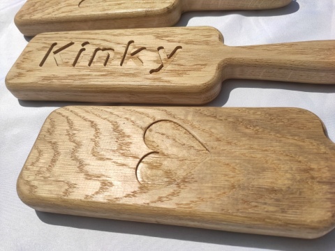 Drewniane packi do klapsów z grawerem „Kinky” i sercem, wykonane z litego dębu, leżące na białym tle – gadżet erotyczny BDSM Drewniane packi do klapsów z grawerem „Kinky” i sercem, wykonane z litego dębu, leżące na białym tle – gadżet erotyczny BDSM