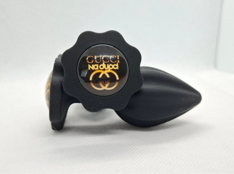 Czarny korek analny „Gucci na dupci” – silikonowy butt plug z ozdobną grafiką w złotym kolorze.